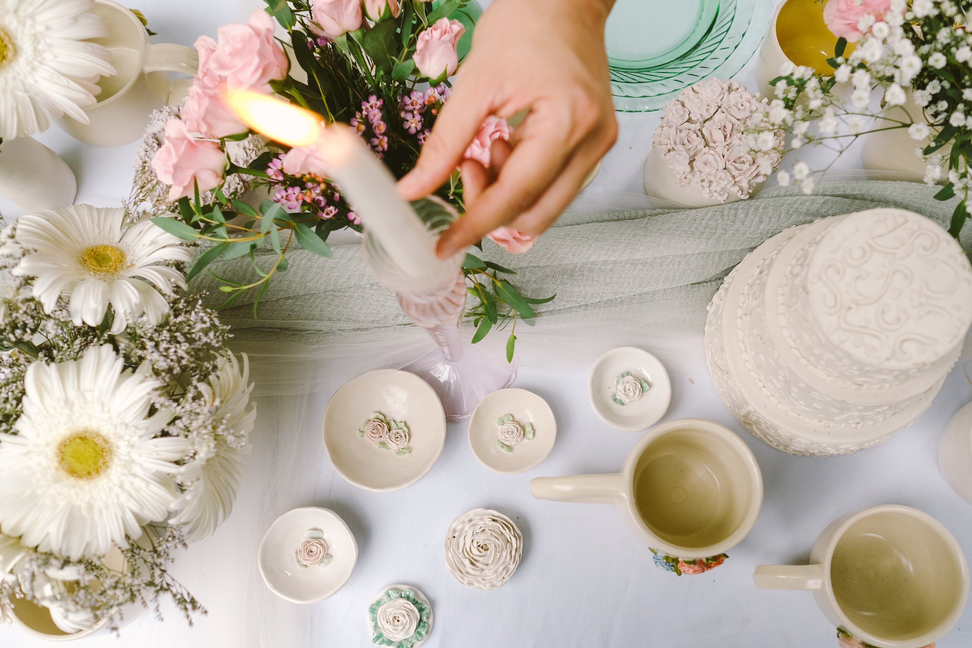 Hand positioning a candle among flowers and ceramic items on a table.